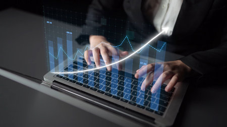 A business professional engages in financial analysis using a laptop, featuring digital graphs that...