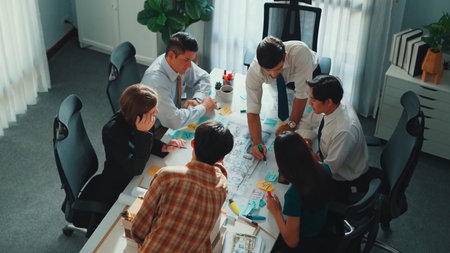 Group of diverse team planning strategy while sitting at table with project plan. Top aerial view of...