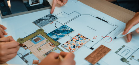 A group of diverse individuals examines a detailed architectural floor plan, highlighting areas for...