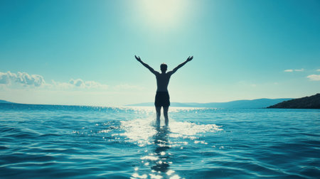 A man stands in the ocean with arms raised, enjoying the warm sunlight. The scene captures a sense of freedom and tranquility against a stunning horizon, ideal for portraying joy and adventure inの素材