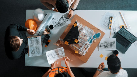 Top view of manager handing blueprint to professional engineer team at meeting table with house...