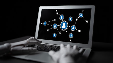 A robotic hand reaches towards a laptop screen showing a network of connections, representing the...
