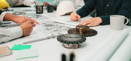 A team of engineers engages in a focused discussion over technical drawings and mechanical designs in a bright and modern office setting, showcasing collaboration and innovation.の写真素材
