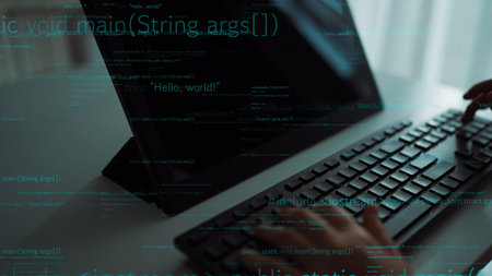 A close-up of hands typing on a sleek keyboard while coding text appears on the screen in a modern...