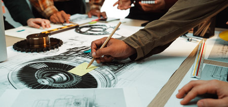 A dynamic team collaborates in a creative workspace, surrounded by engineering drawings and sketches, highlighting the design process and teamwork in action.の写真素材