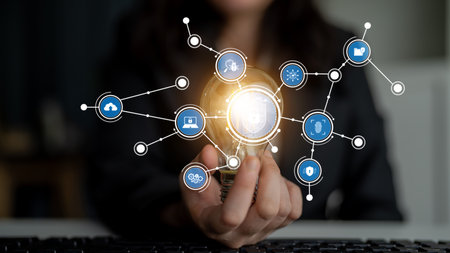 A person holds a glowing light bulb, symbolizing creativity and innovation, while various digital...