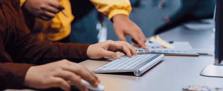 A closeup view of hands at a computer in a vibrant office setting, showcasing professionals...
