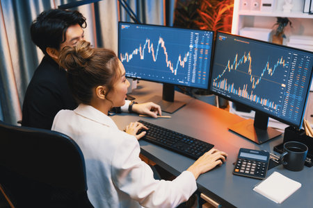Smiling Asian business traders pointing to dynamic stock exchange data screen profit value online...