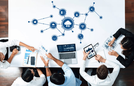 A top-down view of a business team collaborating on cloud computing strategies, using laptops and...