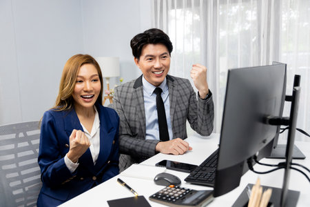 Successful smiling Asian business partners raising fist up together in profitable project job in...