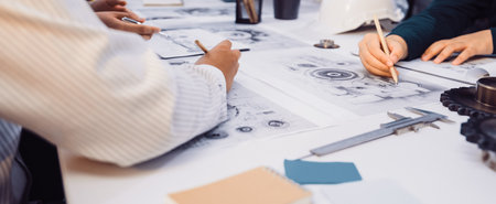 A focused group of engineers collaborates on technical drawings, utilizing tools and notebooks on a...