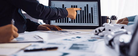 A professional business team collaborates in a modern office, analyzing graphs and charts displayed...