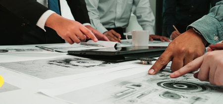 A diverse team collaborates on a technical project, discussing blueprints and using a tablet in a...