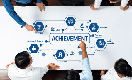 A group of professionals collaborates on a table, pointing at visuals representing achievement,...