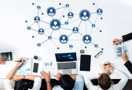 A diverse group of professionals collaborates over a workspace featuring digital connections. They...