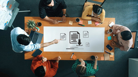 A diverse team collaborates on project planning in a modern office, surrounded by laptops and...