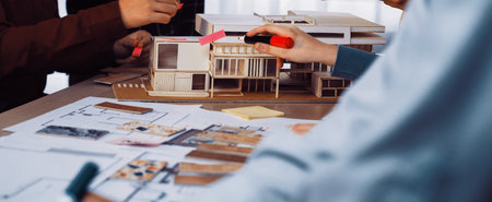 A group of professionals engages in an architectural design session, using a scale model, sticky...