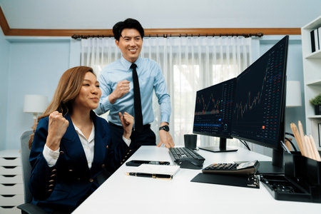 Successful smiling Asian business partners raising fist up together in profitable project job in...