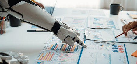 A futuristic robot arm collaborates with a human hand over business reports on an office desk,...