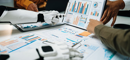 Human and robotic hands engage in a collaborative analysis of business data, showcasing graphs and...