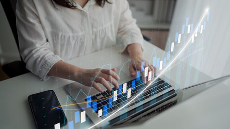 A professional office worker engages with a laptop, analyzing financial data. A digital stock chart...
