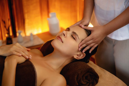 Caucasian woman enjoying relaxing anti-stress head massage and pampering facial beauty skin recreation leisure in warm candle lighting ambient salon spa in luxury resort or hotel. Quiescentの写真素材