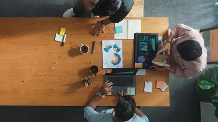 Top view of skilled project manager talking about financial graph to investors while sitting at meeting table with data analysis document. Diverse team discussing and brainstorming idea.の写真素材