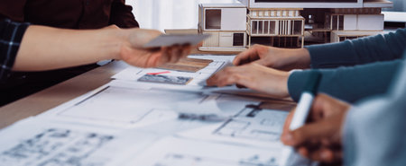 A diverse group of professionals engaged in an architecture design session, collaborating on blueprints, sketches, and models in a modern workspace setting, showcasing creativity and teamwork.の写真素材