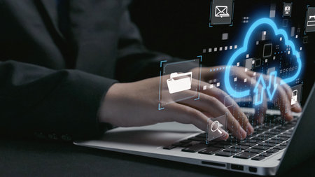 A close-up of hands typing on a laptop keyboard, showcasing cloud technology icons and digital symbols that represent data management and online communication essentials.の写真素材