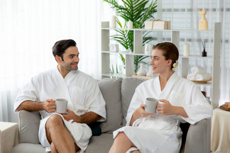 Beauty or body treatment spa salon vacation lifestyle concept with couple wearing bathrobe relaxing with drinks in luxurious hotel spa or resort room. Vacation and leisure relaxation. Quiescentの写真素材