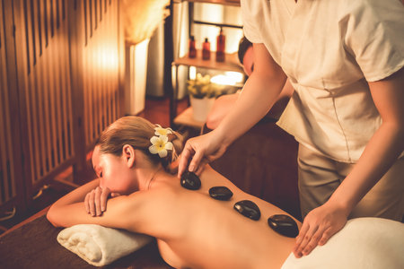 Hot stone massage at spa salon in luxury resort with warm candle light, blissful woman customer enjoying spa basalt stone massage glide over body with soothing warmth. Quiescentの写真素材