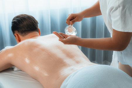 Masseur hands pouring aroma oil on man back. Masseuse prepare oil massage procedure for customer at spa salon in luxury resort. Aroma oil body massage therapy concept. Quiescentの写真素材