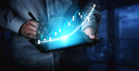 A business professional carefully analyzes financial data displayed on a digital tablet, showcasing vibrant graphs and charts in a modern office setting.の写真素材