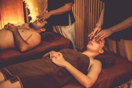 Couple customer enjoying relaxing anti-stress head massage and pampering facial beauty skin recreation leisure in warm candle lighting ambient salon spa in luxury resort or hotel. Quiescentの写真素材