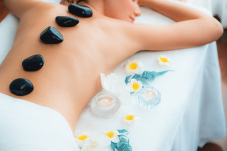 Hot stone massage at spa salon in luxury resort with day light serenity ambient, blissful woman customer enjoying spa basalt stone massage glide over body with soothing warmth. Quiescentの写真素材