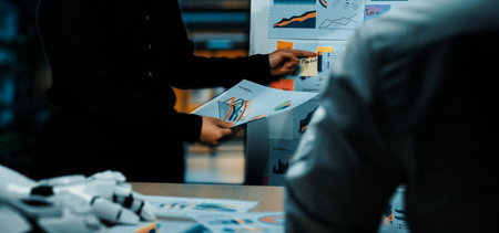 Professionals collaborate in a modern office, discussing printed reports with graphs and charts, emphasizing data analysis and teamwork for effective decision-making.の写真素材