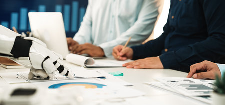A human team collaborates with a robot in a modern office, analyzing financial charts and discussing data. This scene highlights the fusion of technology and teamwork in business.の写真素材