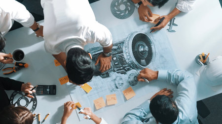 Top view of engineer team writing idea on sticky notes at meeting while discussing about turbine engine or electric generator at meeting table with metal gear, calculator and equipment.の写真素材