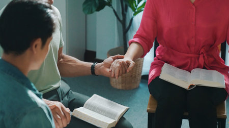 Top down view of diverse calm people holding hand and sitting in circle with bible book on lap. Faithful christian prayer clasp hand and praying to god together with faith. Focus on hands. Symposium.の写真素材