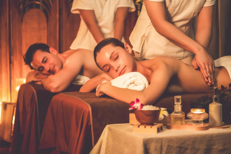 Caucasian couple customer enjoying relaxing anti-stress spa massage and pampering with beauty skin recreation leisure in warm candle lighting ambient salon spa at luxury resort or hotel. Quiescentの写真素材