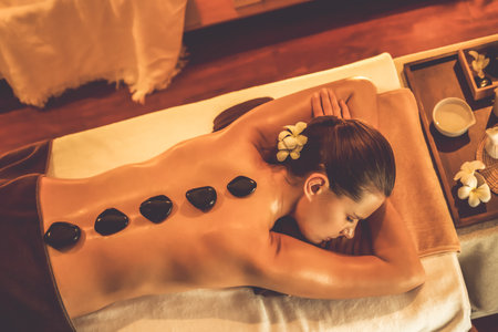 Panorama top view hot stone massage at spa salon in luxury resort with warm candle light, blissful woman customer enjoying spa basalt stone massage glide over body with soothing warmth. Quiescentの写真素材