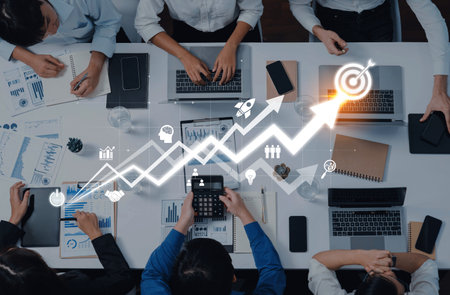 A collaborative group of professionals engaged in financial analysis with laptops and documents, showcasing teamwork and strategic planning in a modern office.の写真素材