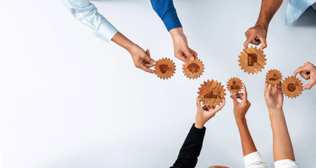 Hands reaching for wooden gears symbolize collaborative management and innovative strategies in a professional office setting, showcasing teamwork and shared goals.の写真素材
