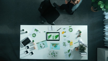 Top down view of project manager walking around meeting table with green business element. Aerial...