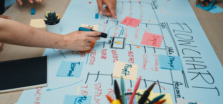 A dynamic scene of teamwork featuring hands engaged in creating a flowchart on a table. Bright...