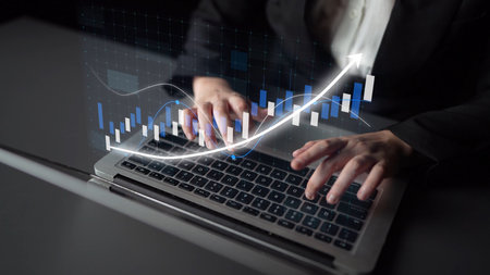 A business professional engages in financial data analysis on a laptop, showcasing digital graphs and charts that highlight growth trends and market performance.の写真素材