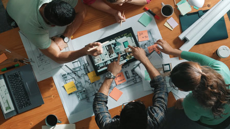Top down view of civil engineers using tablet to design house structure while sitting at table with...