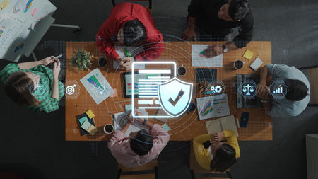 A diverse business team gathers around a table to discuss data protection strategies, featuring digital security icons and colorful charts in a modern office setting. Rasterの写真素材