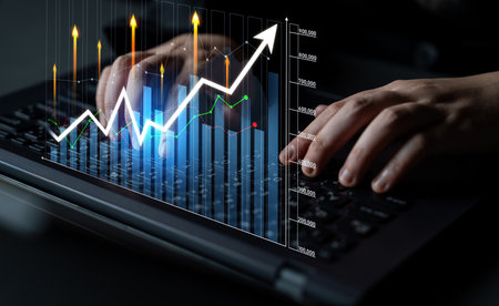 A close-up view of hands typing on a laptop keyboard with dynamic digital graphs representing...