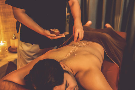 Man customer having exfoliation treatment in luxury spa salon with warmth candle light ambient. Salt scrub beauty treatment in Health spa body scrub. Quiescentの写真素材